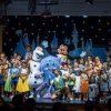 Gruppo di bambini e mascotte su un palco colorato.