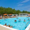 Piscina affollata con sdraio e ombrelloni arancioni.