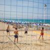 Persone giocano a beach volley sulla sabbia con il mare sullo sfondo.