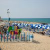 Spiaggia con ombrelloni blu e bianchi, area giochi recintata e mare calmo.