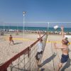 Partita di beach volley con giocatori in movimento mentre uno salta per colpire la palla.