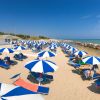 Spiaggia con ombrelloni blu e bianchi e lettini, vicino al mare con cielo sereno.