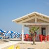 Chiosco bianco sulla spiaggia con sedie rosse. Ombrelloni blu e bianchi sullo sfondo.
