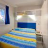 Camera con letto matrimoniale, copriletto a strisce gialle e blu, mensole e finestre.