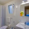 Bagno bianco con doccia, finestra aperta, specchio, lavandino e vaso con fiori.