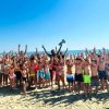 Grande gruppo di bambini sulla spiaggia con le mani alzate.