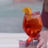 Mano con cocktail arancione in piscina.