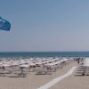 Spiaggia con ombrelloni bianchi e bandiera blu.